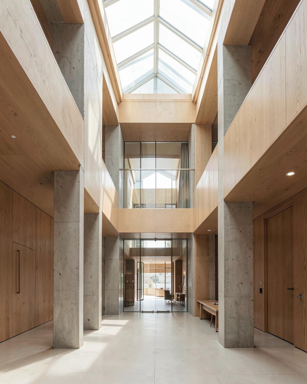 A calm commercial atrium with concrete columns and oak panelling under a glass roof